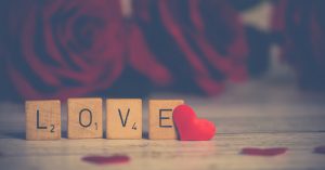 Scrabble letters the spell out the word love with a heart and rose petals in the background | Gunther Kia