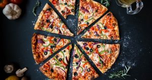 Pizza sliced in 8 pieces, one piece with a bite taken and extra ingredients off to the side | Gunther Kia