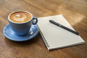 Coffee cup and journal on a table | Gunther Kia