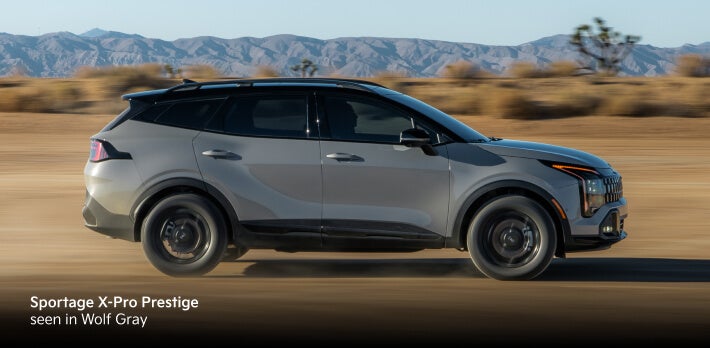 2026 Kia Sportage X-Pro Prestige in Wolf Gray, side profile driving through a desert landscape with mountains.