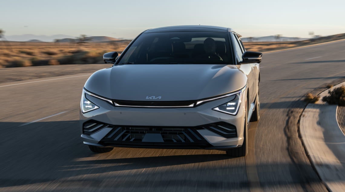 Front view of a silver Kia EV6 driving on an open road with a desert landscape in the background.