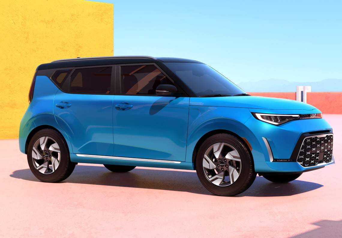 Blue Kia Soul parked in a colorful outdoor setting, featuring a black roof, distinctive LED headlights, and bold geometric styling.